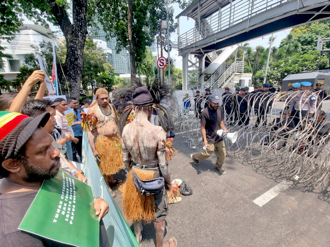 Security forces watch from behind barbed wire as indigenous Papuans from Merauke in the Indonesia-ruled Melanesian region protest in Jakarta