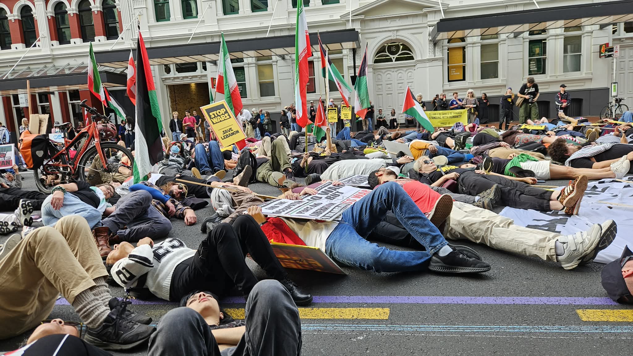 Protesters in the "die-in" in the street outside the US Consulate in Auckland marking the slaughter of 168 Iranian schoolgirls by US bombs in Minab on the opening day of the war