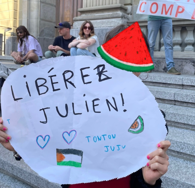 Julien Blondel's niece holds a "free Julien!" placard in French with a Palestinian watermelon logo